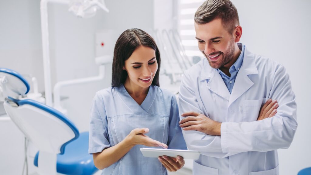Zahnarzt und Assistentin betrachten den Bildschirm eines digitalen Tablets